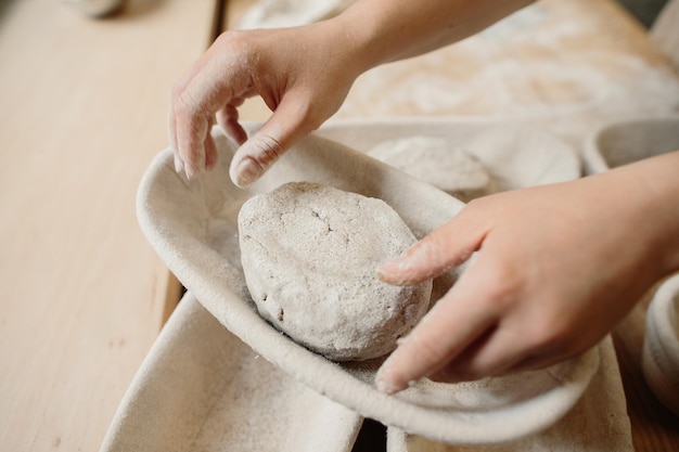 Женщина-пекарь замешивает тесто и кладет его в деревянную форму Концепция пекарни