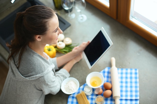 Женщина печет дома по рецепту на планшете