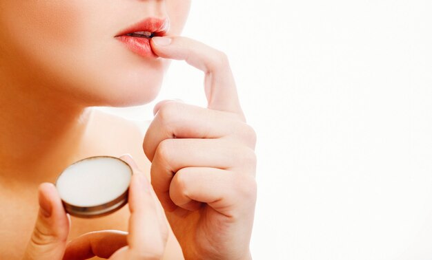 woman and balm, close-up woman is applying balm to the lips on white wall