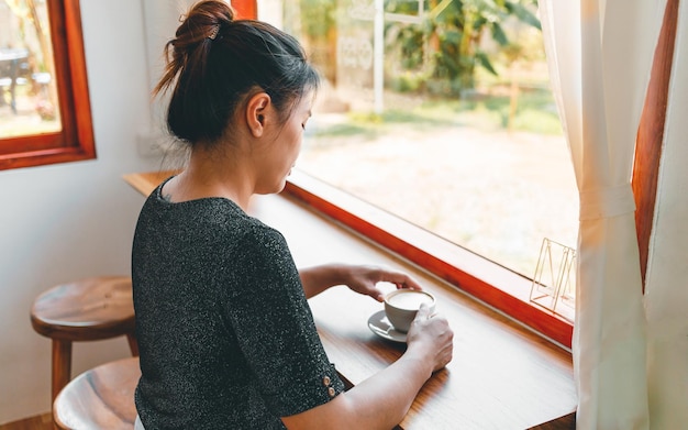 Woman at the bar counter coffee shop holding a cup of coffee smiling relaxed in a cafe