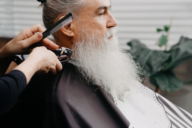 Woman barber cutting hair to an aged bearded man