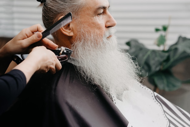 Barbiere donna che taglia i capelli a un uomo barbuto invecchiato