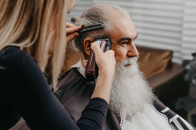 Woman barber cutting hair to an aged bearded man