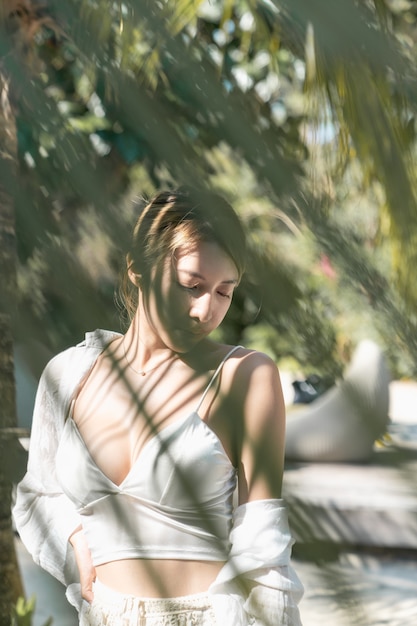 Woman bare her shoulders with palm tree leaf shadow on face.