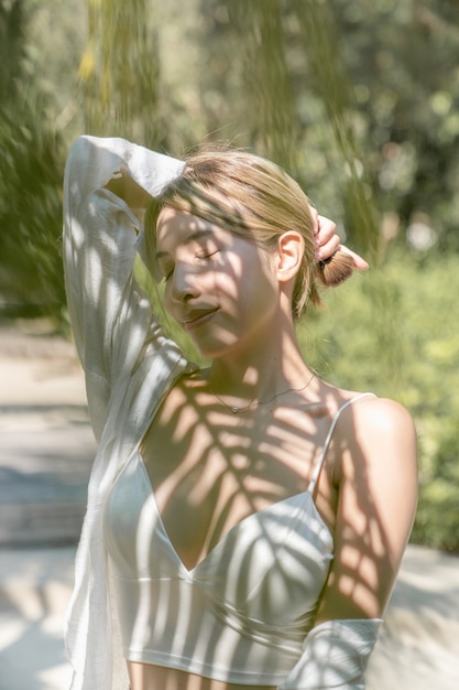 Woman bare her shoulders with palm tree leaf shadow on face.