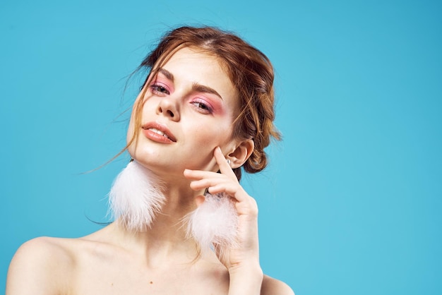 Woman bare shoulders fluffy earrings fashion bright makeup blue background High quality photo