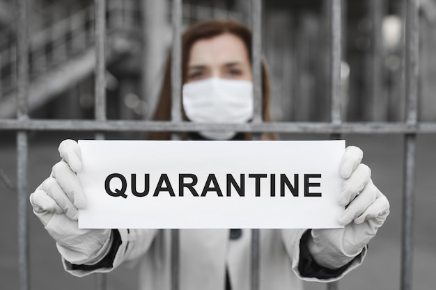 A woman behind bars in isolation holds a placard reading quarantine . Message for the prevention of coronavirus covind-19.