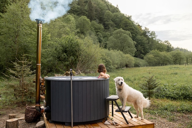 Woman bathing in hot tube while resting with her dog on nature