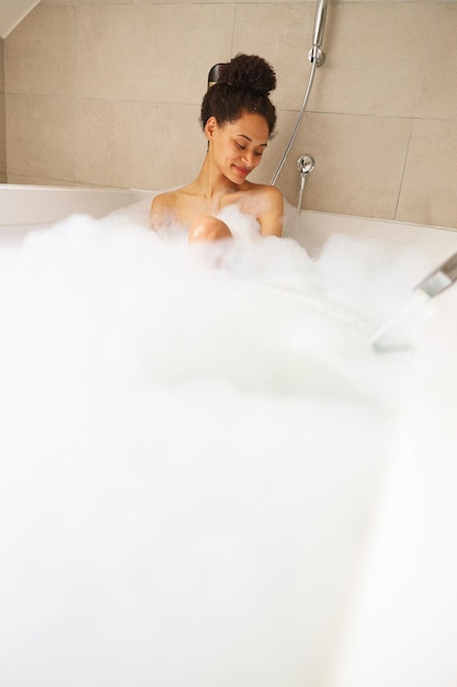 A woman bathing in a tub filled with foam her head covered in bubbles