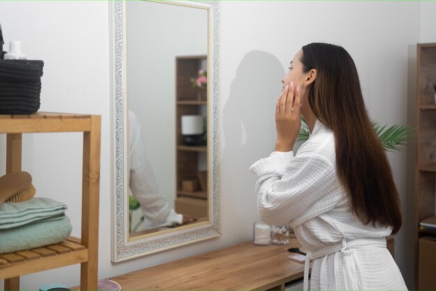 woman in a bathrobe at home explores a beauty skincare concept looking to bathroom mirror