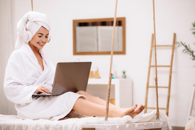 Woman in bathrobe uses laptop in bedroom