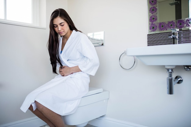 Woman in bathrobe with bellyache in toilet