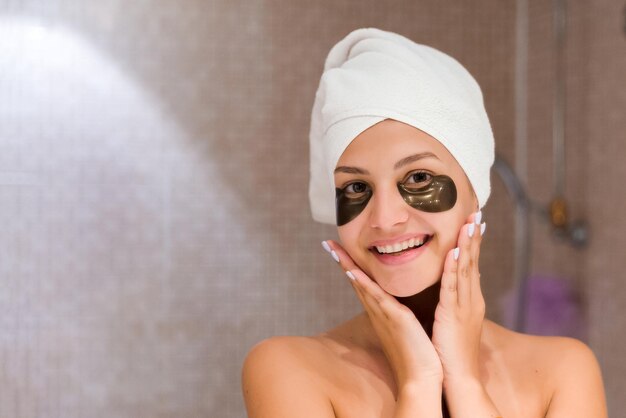 Woman in bathroom applying black eye patches Skin care and spa morning concept