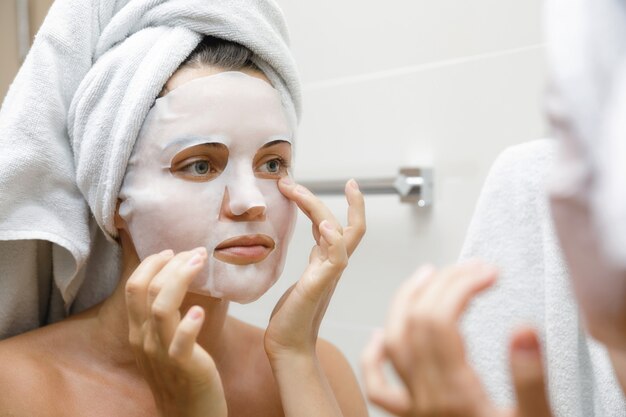 Woman in bathroom is applying facial sheet mask