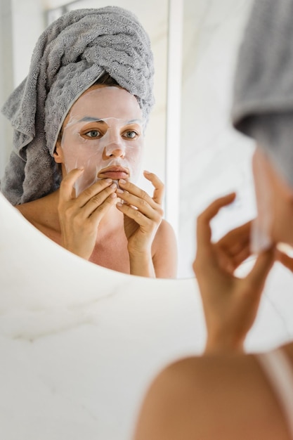 Woman in bathroom with applied sheet mask on her face looking in the mirror