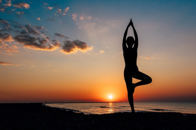 Woman on the beach at dawn in yoga assana