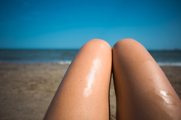 A woman on the beach smears her feet with sunscreen lotion from an orange tube Skin care UV protection sunscreen Beach holidays