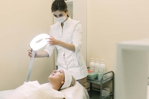 woman beautician adjusts the light lamp above the patient