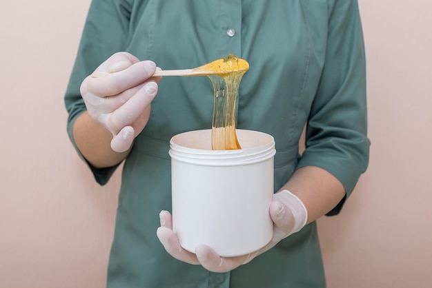 A woman beautician holds a jar of sugaring paste.