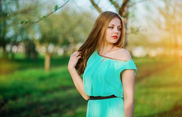 Woman in a beautiful long turqoise dress posing on a meadow in garden.