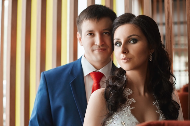 Woman in a beautiful white dress and a man in a blue suit hugging near the window. Loving and affectionate couple