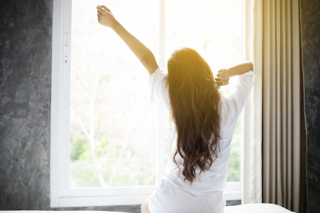 woman Beautiful young smiling sitting on bed and stretching in morning at bedroom 