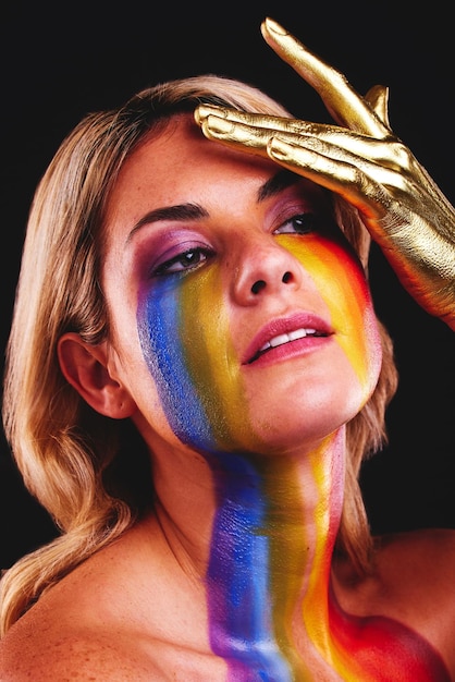 Woman beauty face and gold color paint and cosmetics on skin in studio Female model person on a black background for art deco fantasy and creative rainbow makeup with metallic hand on head