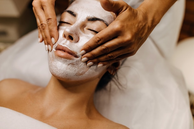 Donna in un salone di bellezza con un massaggio al viso con una maschera in crema scintillante