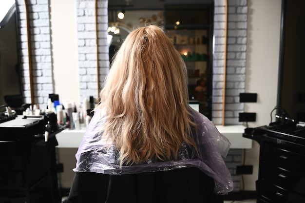 A woman in a beauty salon sits in a hairdressing chair with her hair down, waiting to be treated.