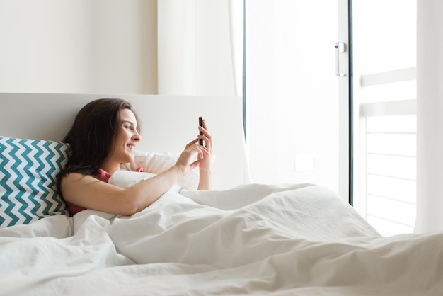 スマートフォンでソーシャルアプリをチェックするベッドの女性