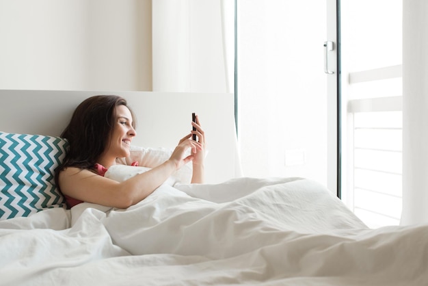 Woman in bed checking social apps with smartphone