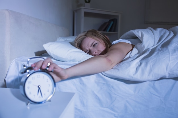 Woman in bed extending hand to alarm clock