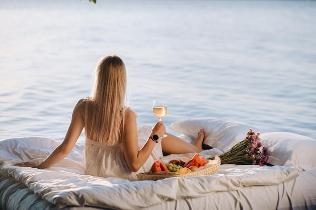 A woman in bed is resting on the seashore with a glass of champagne and fruit