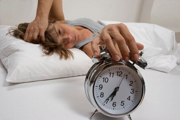 Photo woman in bed turning off alarm clock