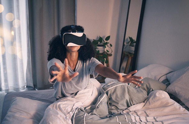 メタバースマトリックスでの夜の自宅とオンラインでの女性のベッドとVRゲーム、挑戦のために手を伸ばす女の子の拡張現実メガネと3Dユーザーエクスペリエンスのビジョン暗い寝室とアパート
