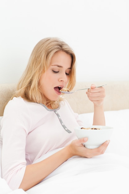 Woman in bed, with her mouth open about to eat a spoon of cereal