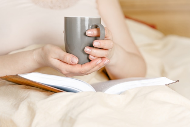 Woman in bed with tea cup and a book. Adult woman reading in the bed.