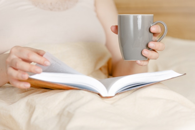 Woman in bed with tea cup and a book. Adult woman reading in the bed.