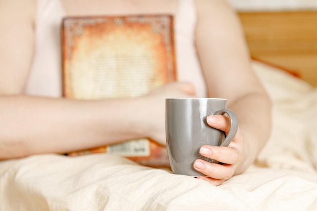 Woman in bed with tea cup and a book. Adult woman reading in the bed.