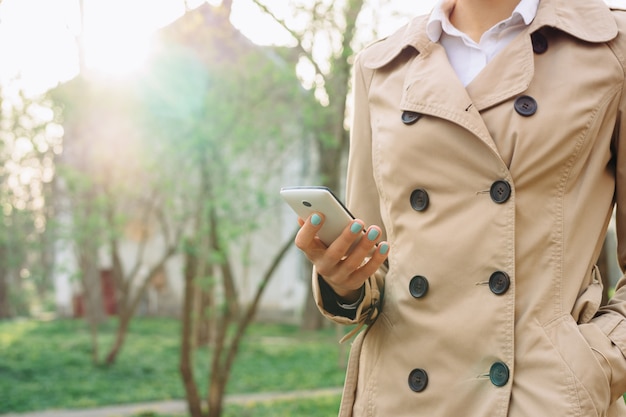 Woman in beige coat holding a mobile phone in park