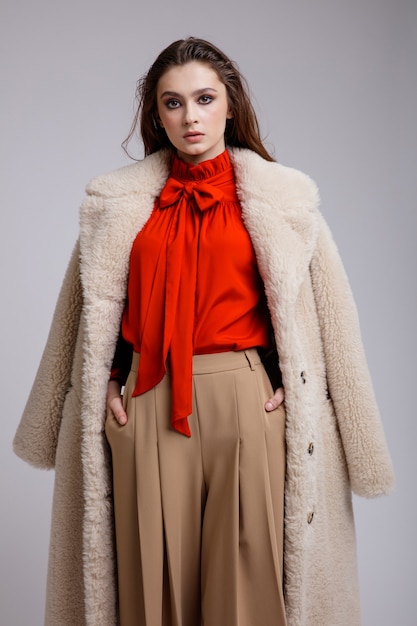 Woman in beige coat long skirt red bow blouse boots on white background Brown hair Studio Shot