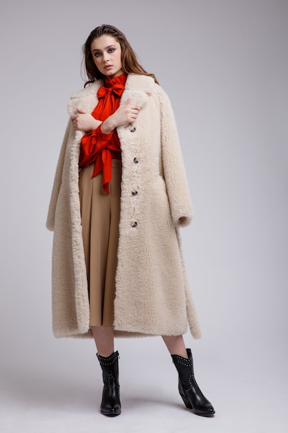 Woman in beige coat long skirt red bow blouse boots on white background Brown hair Studio Shot