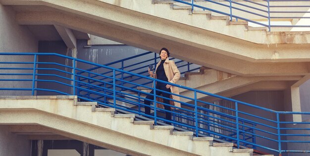 Photo a woman in a beige coat stands on an open staircase and looks ahead person