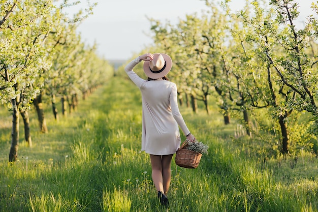 woman in beige dress and hat holding a basket of flowers