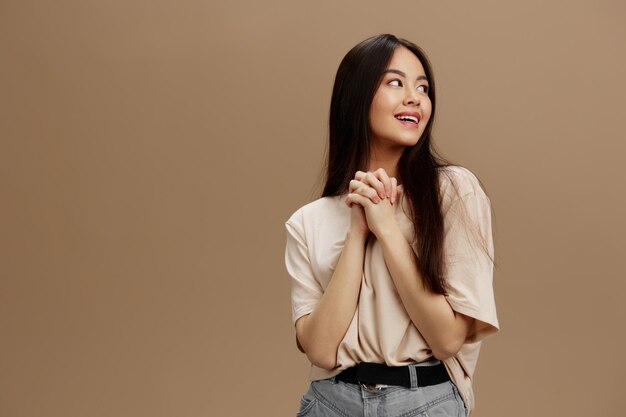 ベージュ色のTシャツを着た女性がポーズをとりファッションのベージュの背景で高品質の写真を撮っています