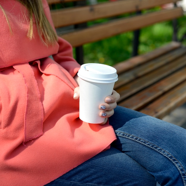 持ち帰り用のコーヒーが付いているベンチの女性