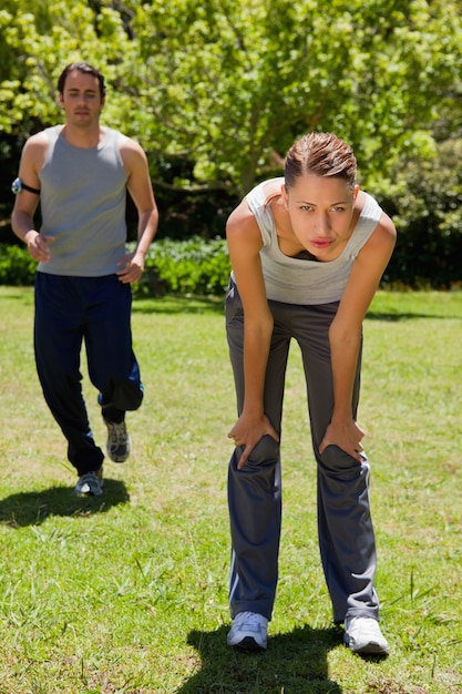 Woman bending over while a man is jogging in the background