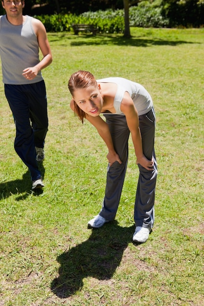 Woman bending over while a man is jogging behind her