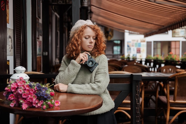 A woman in a beret and a green sweater holds a camera in her hands and takes shoots