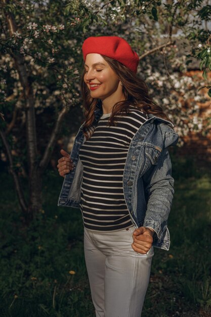 woman in beret and with red lips standing with closed eyes in spring garden